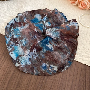 Close-up of a blue and brown vintage floral scrunchie on a stylish wood and fabric backdrop