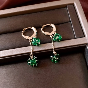 Macro detail of gold earrings featuring emerald green faceted stones and long tassels