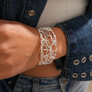 Detail of silver hollow intertwined bangle on female wrist with denim jacket sleeve