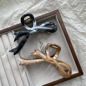 Detailed view of ink marble and amber acrylic bow hair claws on a wooden tray