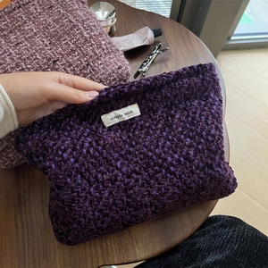 Detailed texture of dark purple woven tweed cosmetic bag with simple wish label