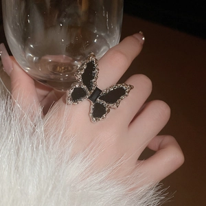 Close-up of elegant silver butterfly ring with black inlay on a hand near a glass