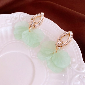 Close-up of light green resin flower earrings with cubic zirconia in a vintage ceramic dish