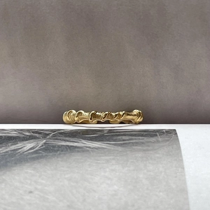 Detail of a minimalist gold twist ring with bamboo texture on a neutral studio background