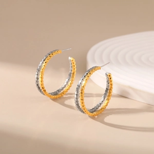 Detailed close-up of geometric gold and silver hoop earrings with faceted metal texture