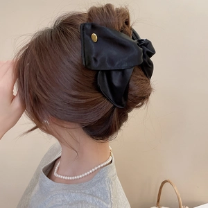 Elegant black satin bow hair claw clip with gold metallic detail worn by a model