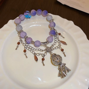 Detail of a purple beaded bracelet with silver metal fringe and a hollow spherical charm
