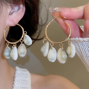 Detail of gold hoop earrings with white shell pendants worn by a model in warm light