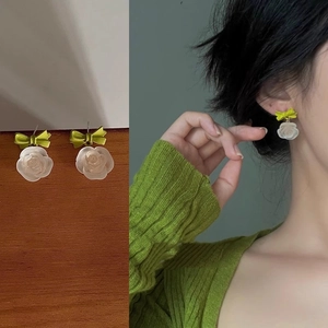 Detail of cream flower earrings with green bows shown on wood and worn by model
