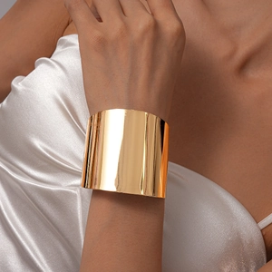 Gros plan d'un bracelet manchette doré poli effet miroir sur fond de soie blanche élégante