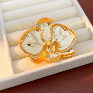 Detailed close-up of a gold-plated orchid brooch with white enamel petals on a velvet box