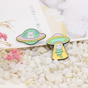 Detailed view of UFO space cat and dog enamel pins on white pebbles and pink flowers