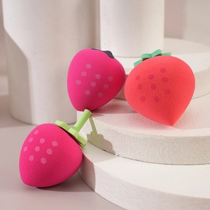 Three strawberry-shaped makeup sponges in red and rose on white display stands