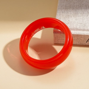 Macro detail of a red resin geometric bangle featuring a marble texture on a warm surface
