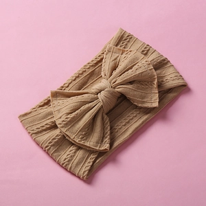 Close-up of tan cable knit baby headband with large bow detail on pink background