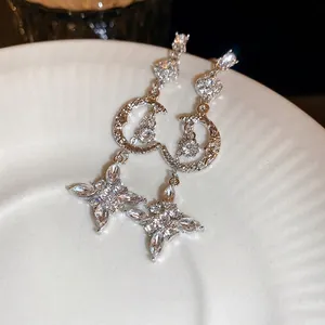 Elegant silver tassel earrings with moon and star zircon motifs on a white porcelain dish