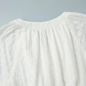 Détail macro de robe blanche brodée avec motif en losange et col rond plissé élégant