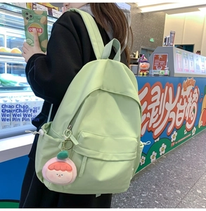 Close-up of light green nylon backpack with pink plush charm in a street style setting
