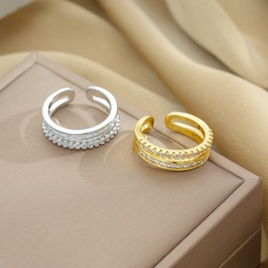 Detail of gold and silver double-row zircon open rings on a beige jewelry box