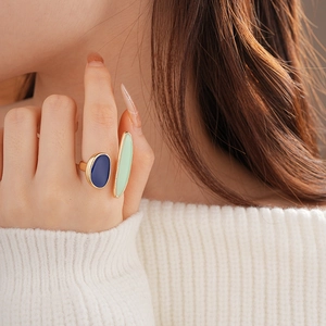 Close-up of geometric gold ring with blue and green enamel shapes on a model hand