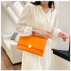 Elegante borsa a busta arancione con fibbia dorata e catena su un abito bianco