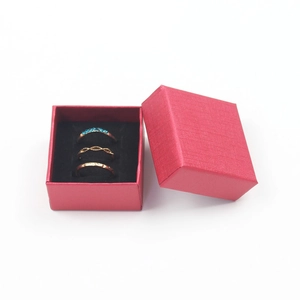 Three gold rings set with one blue stone in a red textured paper jewelry gift box