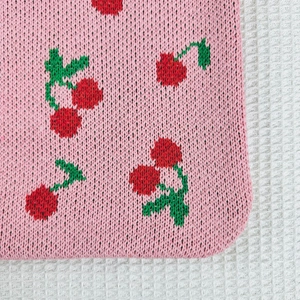 Close-up of pink knitted fabric featuring red cherry patterns and green leaf details