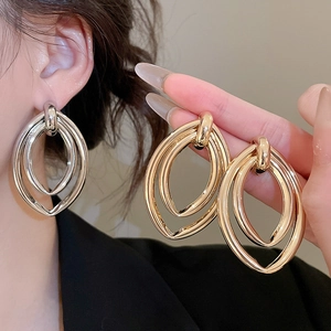 Détail macro de boucles d'oreilles ovales superposées en finitions dorée et argentée