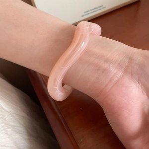 Detail of pink marble pattern resin bangle with an irregular wave design on a female wrist