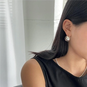 Close-up of high-polish silver C-shape hoop earring worn with a beaded chain necklace