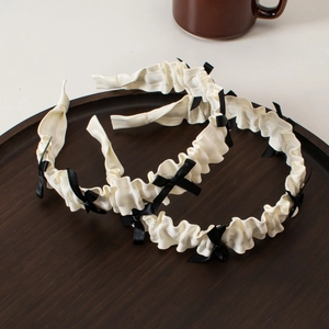 Close-up of white pleated lolita headbands with small black bows on a wooden tray