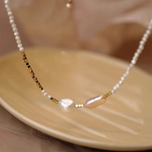 Detail of baroque pearl necklace with gold spacers on a beige ceramic plate