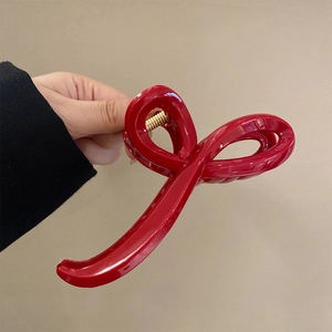 Close-up of a glossy red hair claw clip held against a minimalist beige background