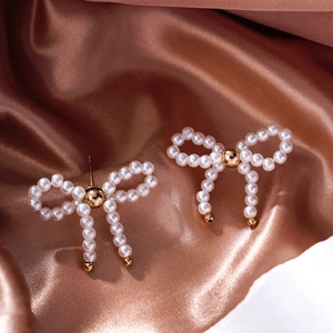 Detail of elegant pearl bow earrings with gold beads on a rose gold silk background