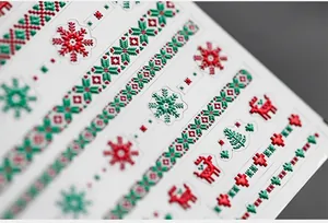 Dettaglio macro di adesivi 3D natalizi per unghie con motivi di renne e fiocchi di neve