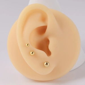 Détail macro de trois boucles d'oreilles boules dorées montrant différentes tailles