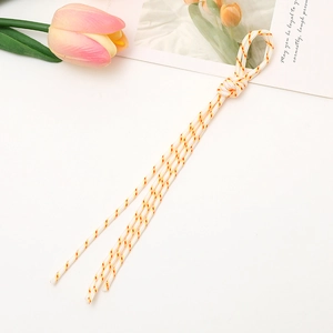 Close-up of white braided phone strap with red and yellow stripes on a desk with tulip