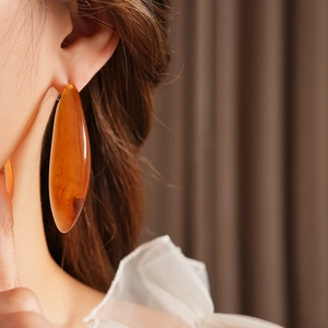 Gros plan de boucles d'oreilles gouttes en résine ambre portées par un mannequin au style chic