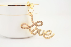 Detail of gold metal LOVE keychain with sparkling rhinestones hanging on a ceramic cup