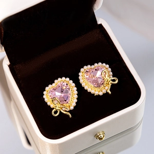 Macro detail of pink crystal heart stud earrings with pearls and a gold bow detail