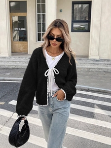 Women's loose black knit cardigan with white bow ties and lace trim in a street style look