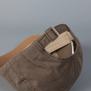 Detail of the brown cotton baseball cap showing adjustable strap and bronze metal buckle