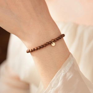 Close-up of minimalist agarwood bead bracelet with a gold metal pendant on wrist
