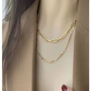 Detail of layered gold stainless steel cross and paperclip chain necklace on model