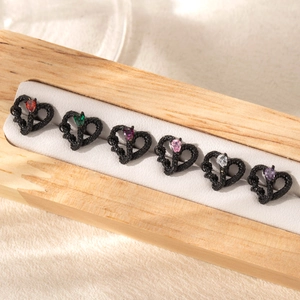 Set of black heart-shaped stainless steel earrings with multi-colored gemstones on a display