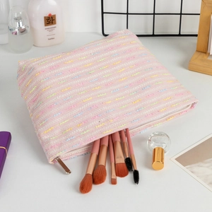 Pink woven vanity bag with colorful threads and matching makeup brushes on white desk