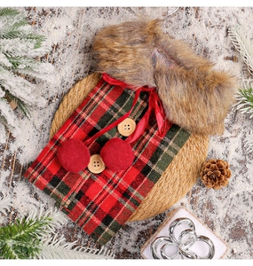 Detail view of red green plaid wine bottle cover with faux fur collar on snowy wood surface