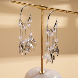 Detail of silver C-hoop earrings featuring long pearl tassels and metal leaf pendants