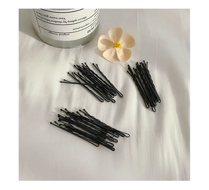Flat lay of multiple black metal bobby pins arranged on soft white fabric background