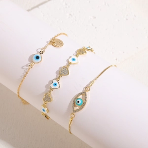 Three-piece gold plated evil eye and heart bracelet set with letter A pendant on white pillar